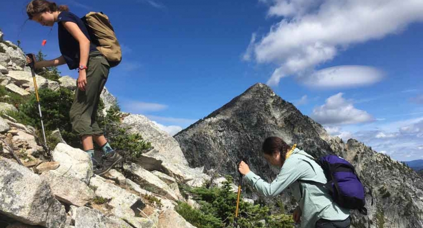 two students ascend over a rocky landscape with a mountain in the background